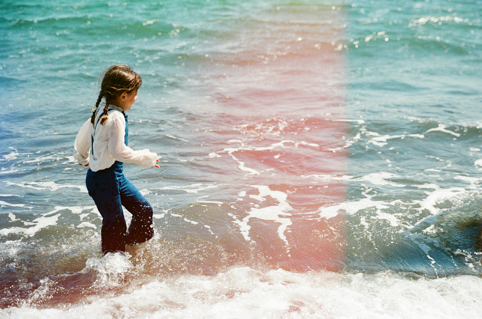 girl running through water at the beach in jean overalls