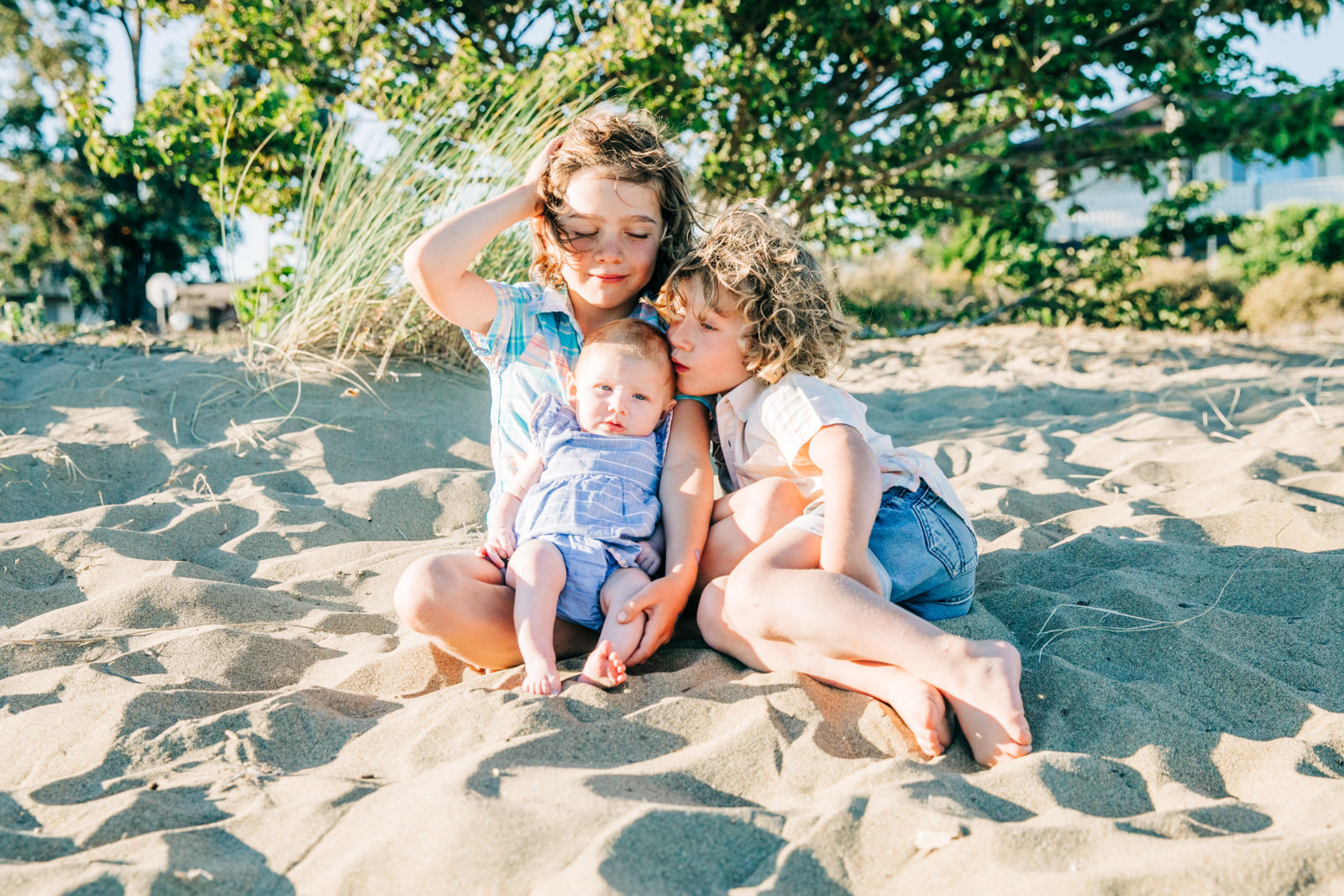 three kids sitting in the sand, older boy holding infant girl