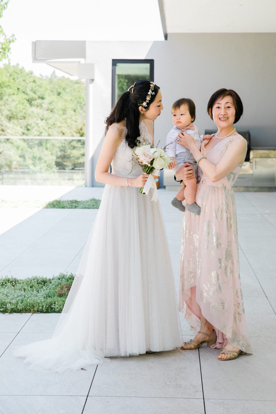 mother of the bride holding grandchild with daughter in wedding dress