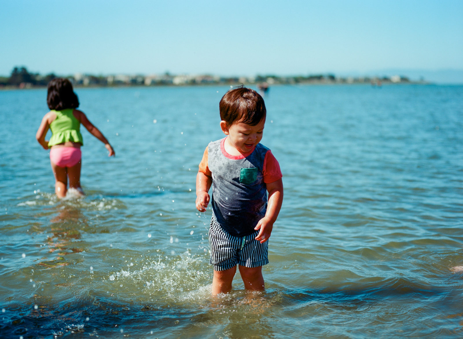 young boy in ocean with sister in background