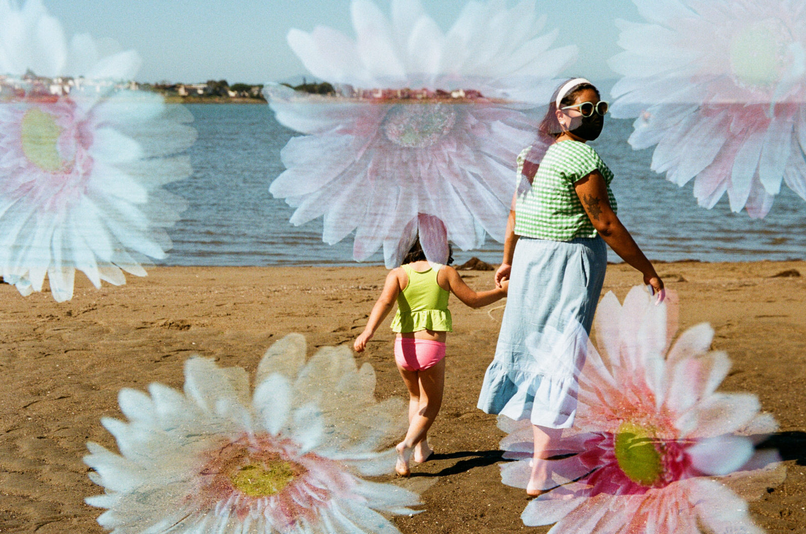 double exposure of daisies and a woman walking toward ocean holding young daughter's hand