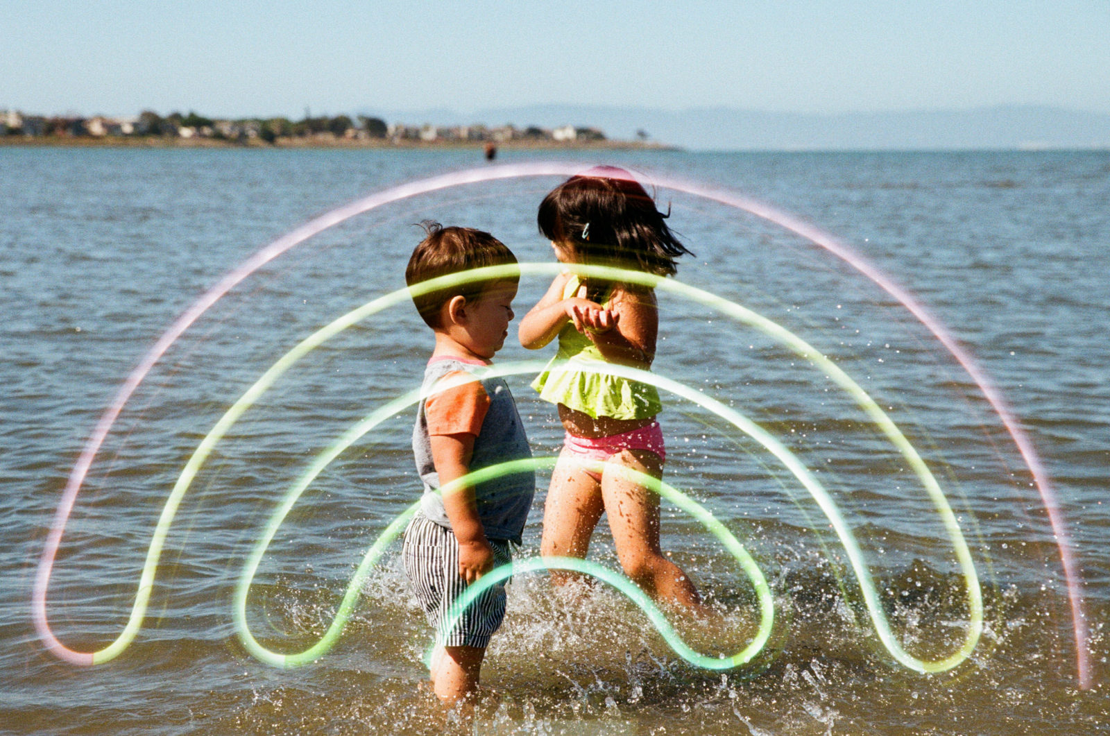 double exposure of rainbow neon and two young kids in ocean