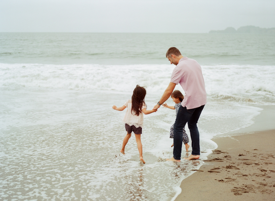 father with two daughters dipping feet in the ocean