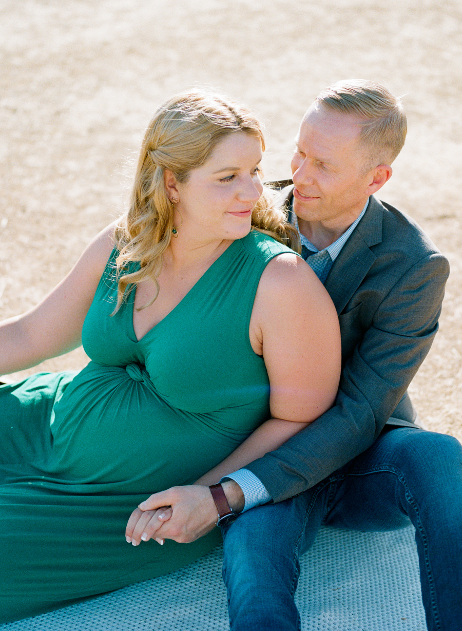 image of pregnant woman in green dress with husband sitting on blanket