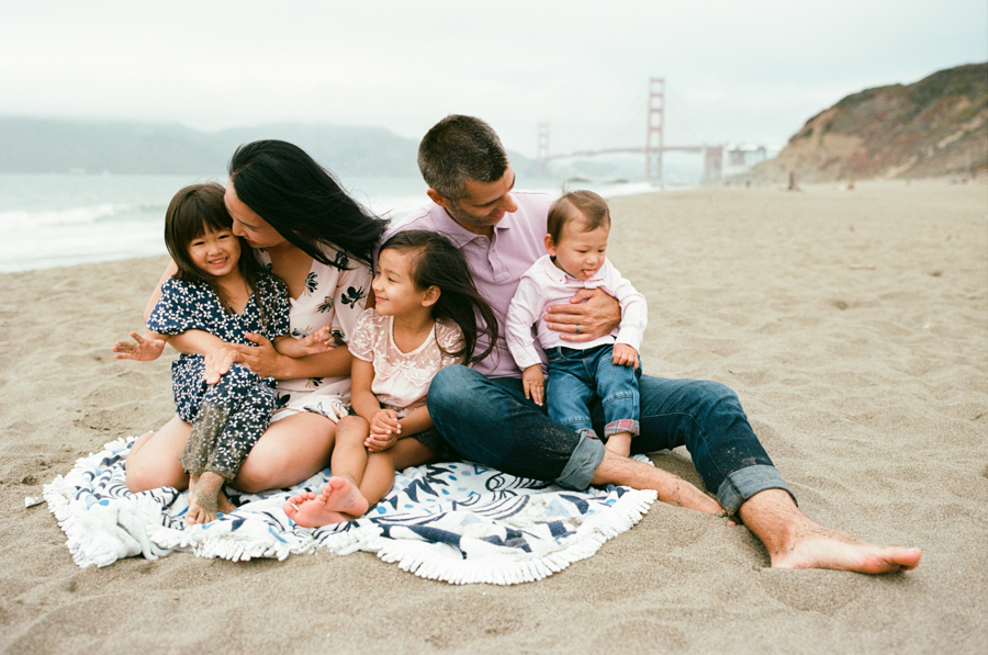 family of five cuddled up on blanket at baker beach san francisco