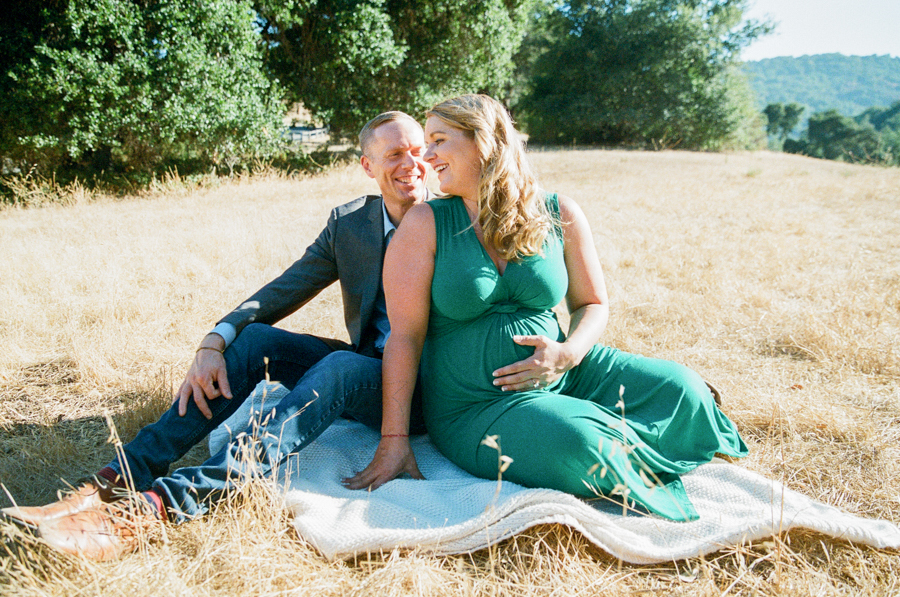 husband and pregnant wife sitting on a blanket in a field