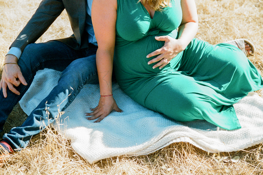 film photo of woman holding pregnant belly while husband sits nearby