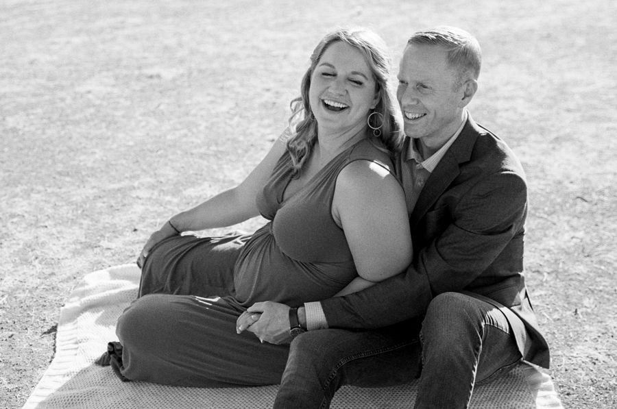 black and white image of husband and pregnant wife sitting on the ground
