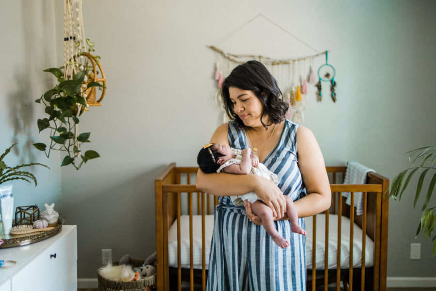 mother holding newborn daughter in her boho nursery
