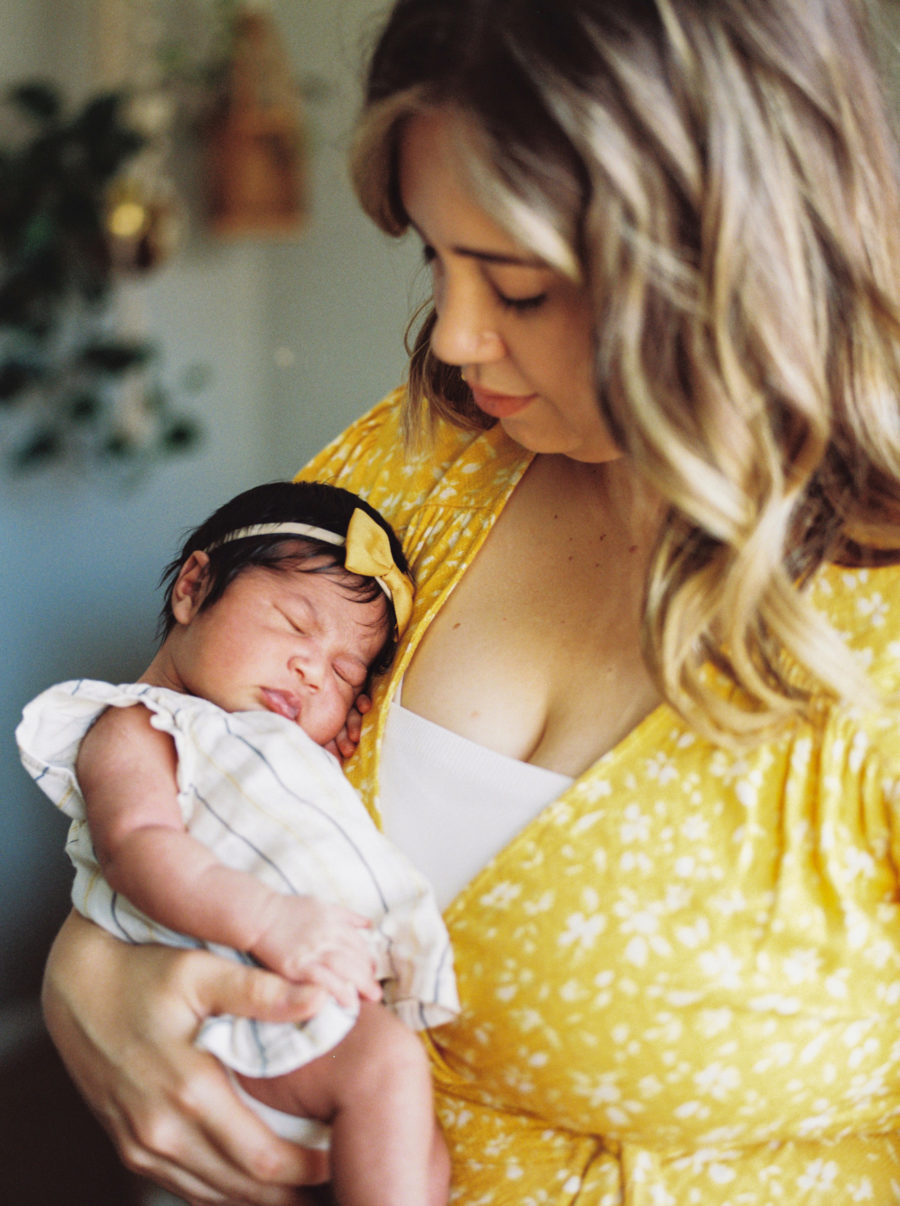 newborn baby girl in yellow bow held by mom in yellow dress
