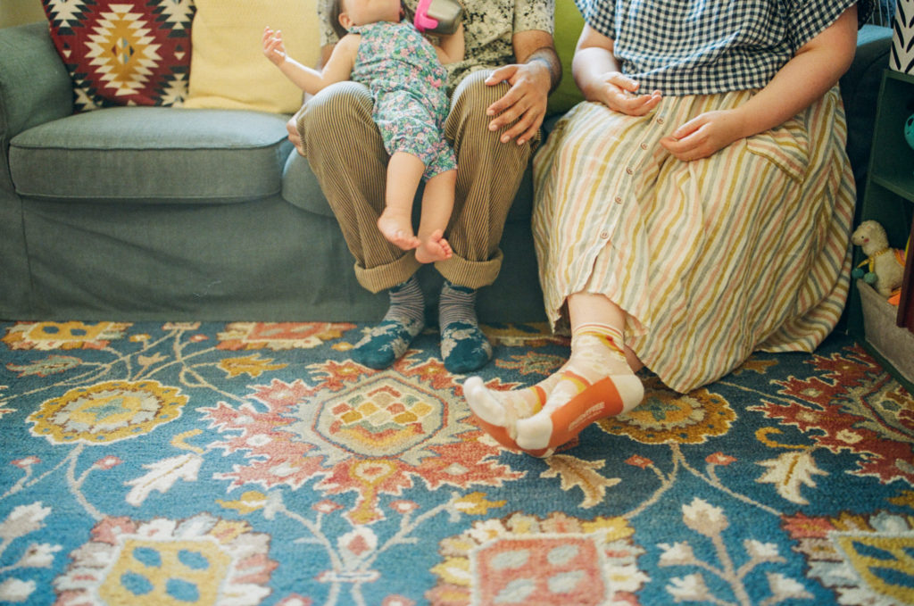 faceless photo of mom dad and baby sitting on couch with floral rug underneath