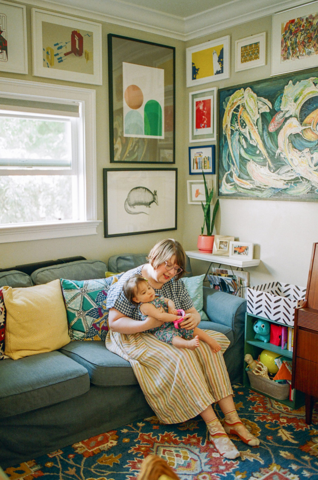 mom and baby sitting on couch with a gallery wall corner behind them