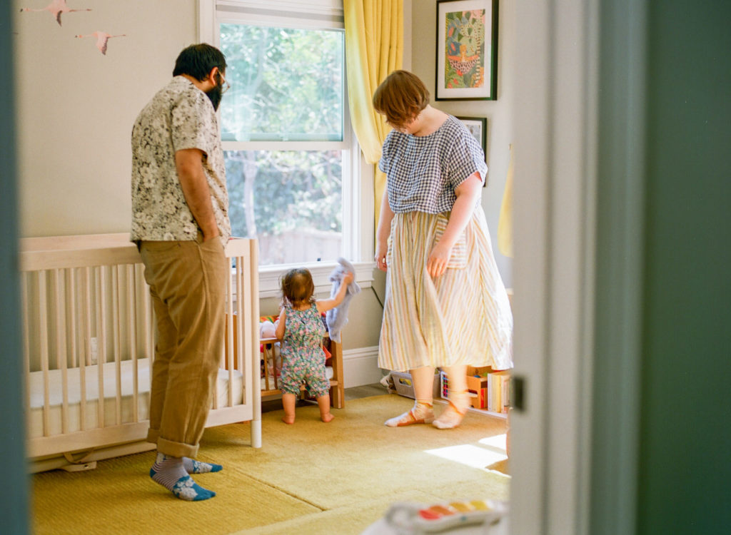 mom dad and baby in nursery with yellow curtains
