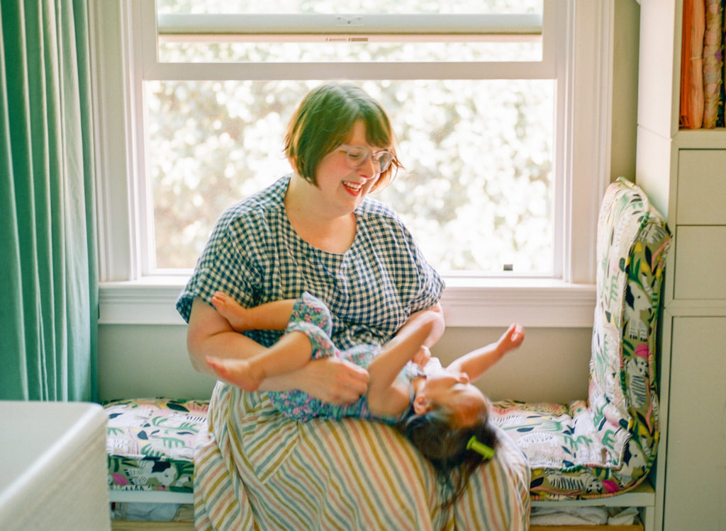 mom sitting on a window seat bench and playing with baby on her lap