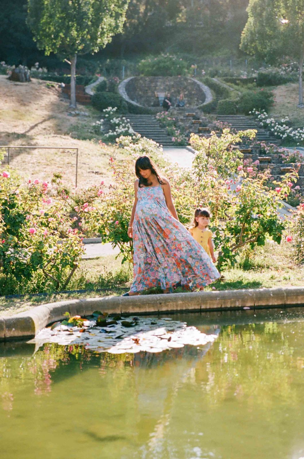 photo of pregnant woman in free people dress with toddler daughter by a pool of water
