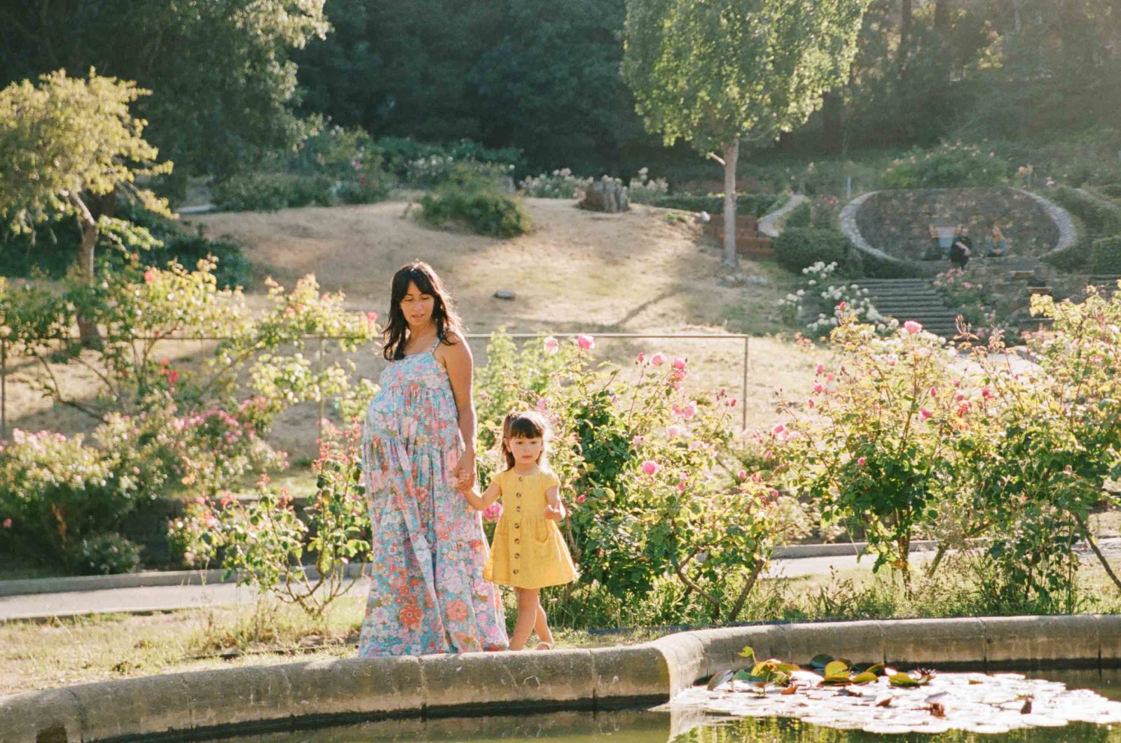 photo of pregnant woman in floral free people maxi dress holding hands with toddler daughter in yellow dress