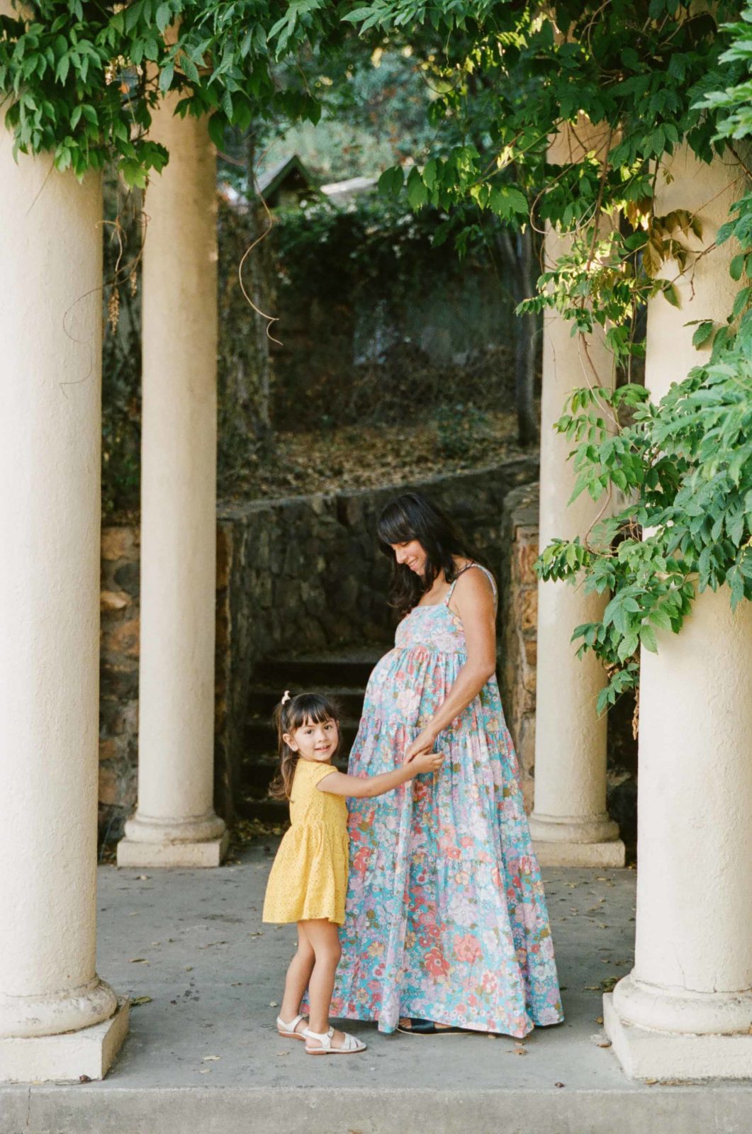 mother and toddler daughter standing between columns at oakland rose garden