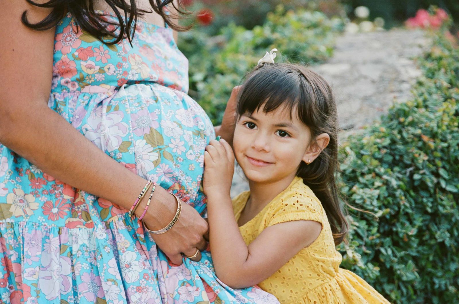 close up of toddler girl in yellow dress leaning into mom's pregnant belly