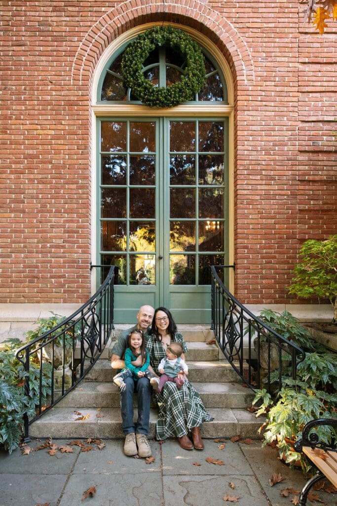 family of four sitting on steps in front of a large picture window in a brick building