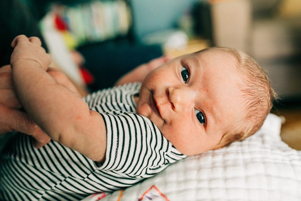 An adorable baby in a striped shirt smiles at the camera during a newborn photography session with Hi + Hello Photo in San Francisco