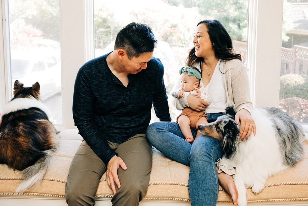 A candid photo of a happy couple with their two dogs and baby during a newborn lifestyle photo shoot at home in the Bay Area