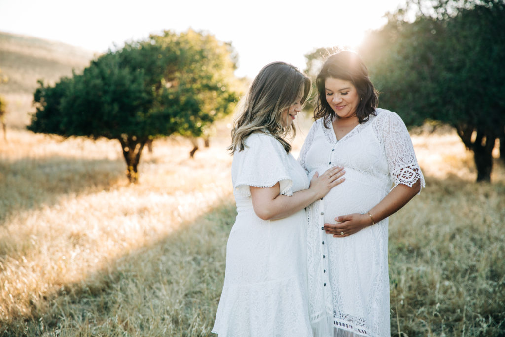 Two women wearing white dresses standing in a field for their maternity session with bay area maternity photographer Hi + Hello Photography