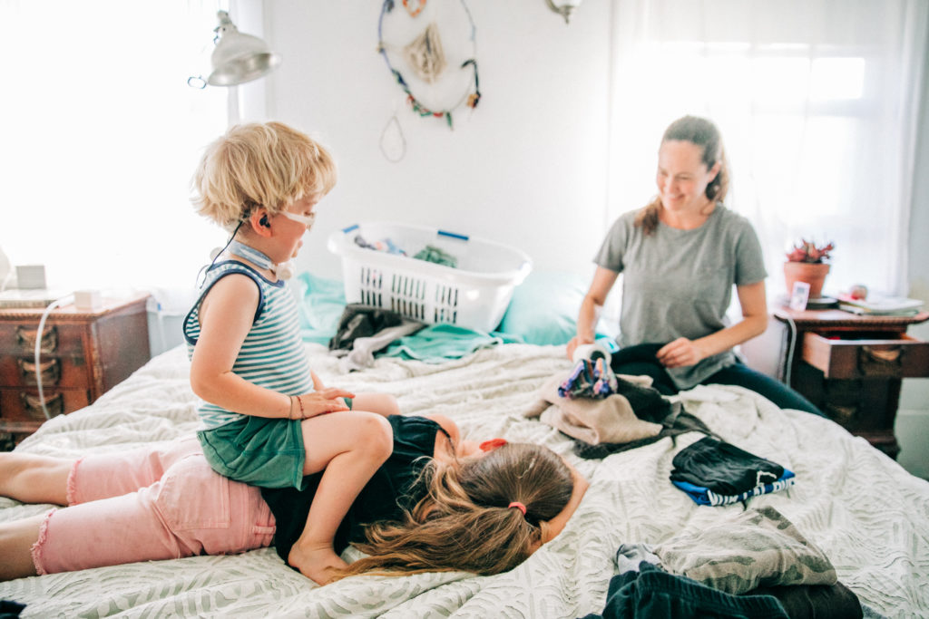 A mother folds laundry while her children play on the bed during a lifestyle family photography session in San Francisco