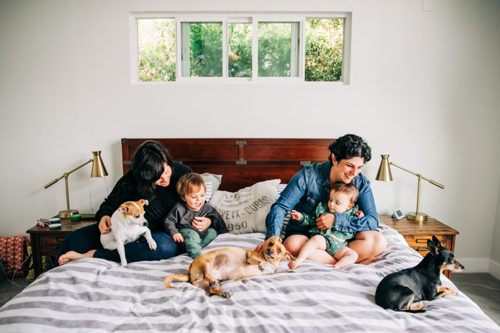 A smiling couple sits in bed with their young children and three dogs for lifestyle family photographs in San Francisco