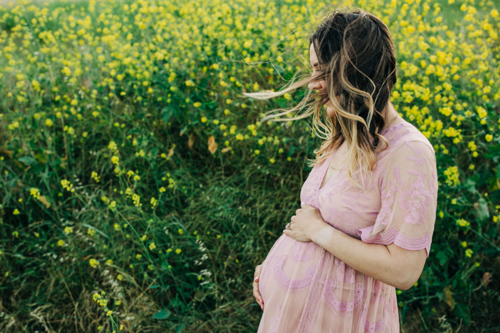A pregnant woman wearing a flowing pink dress stands in a field of flowers during an outdoor maternity photo shoot in San Francisco
