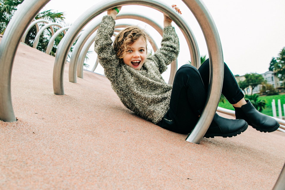 A well-dressed child plays in a park and smiles at the camera during a lifestyle photo session with Bay Area family photographer Hi + Hello Photography