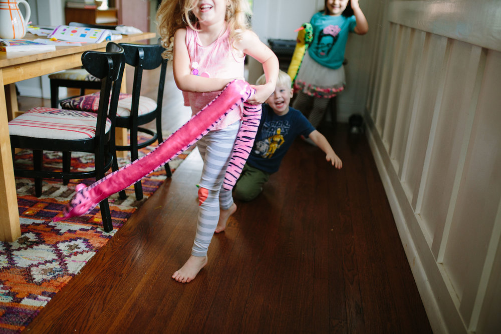 three kids running through house with stuffed snake