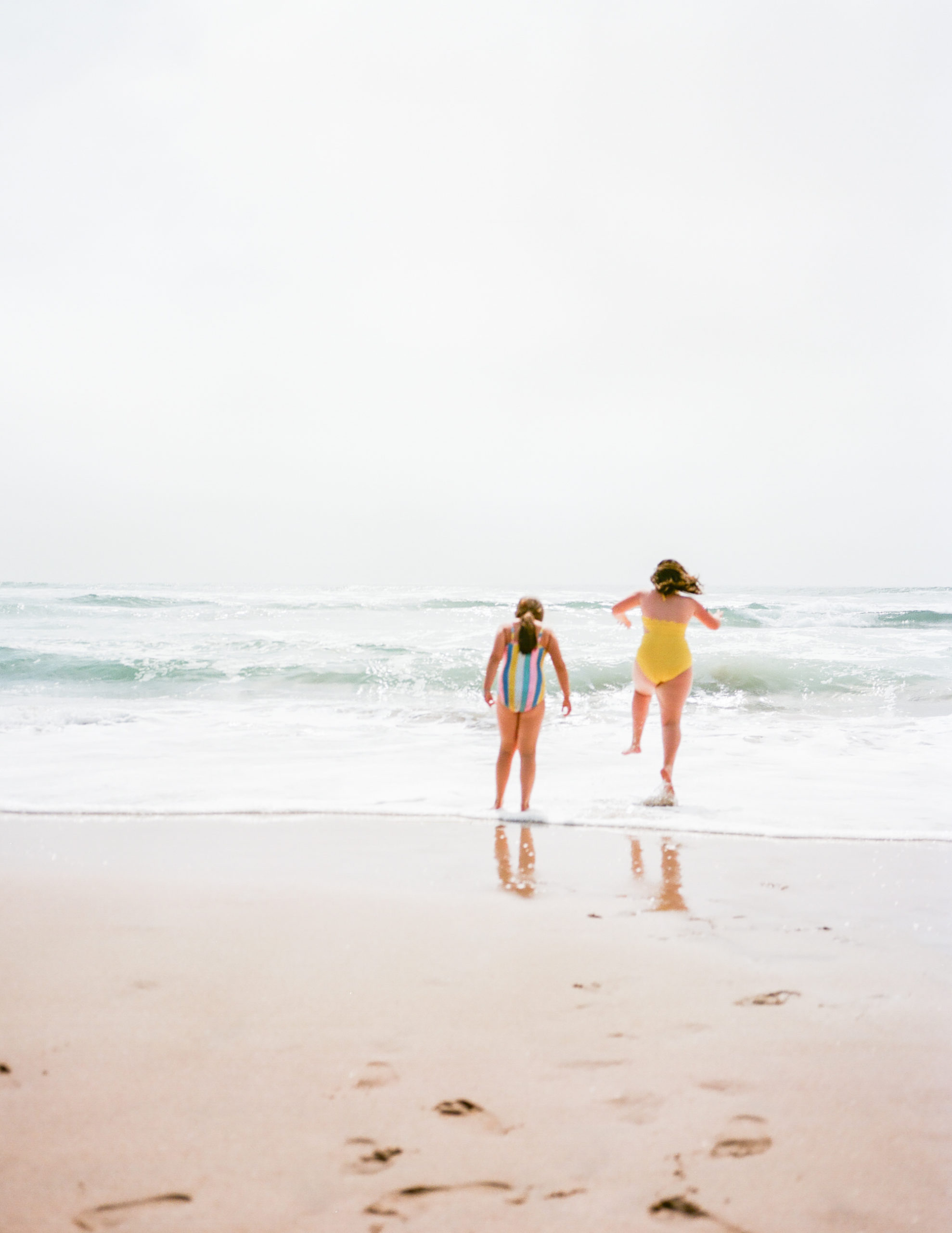 film photo of two girls in bathing suits jumping over waves in ocean