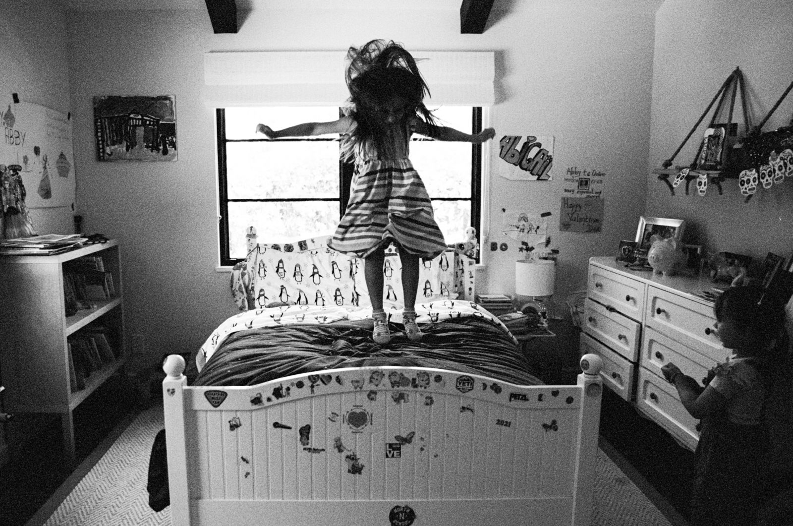 family photos at home of a young girl jumping on her bed which has stickers all over the footboard