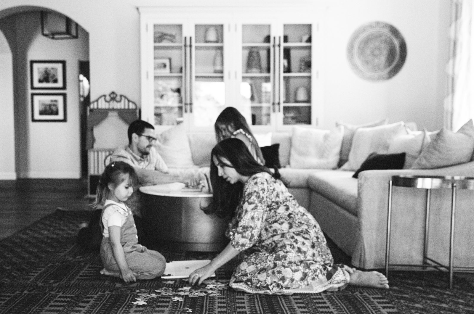 black and white photo of a family at home in their living room playing with a puzzle