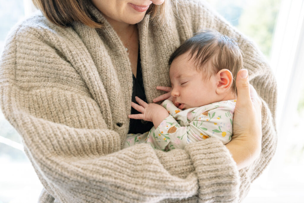 mother in beige cardigan holding squishy newborn baby in floral onesie