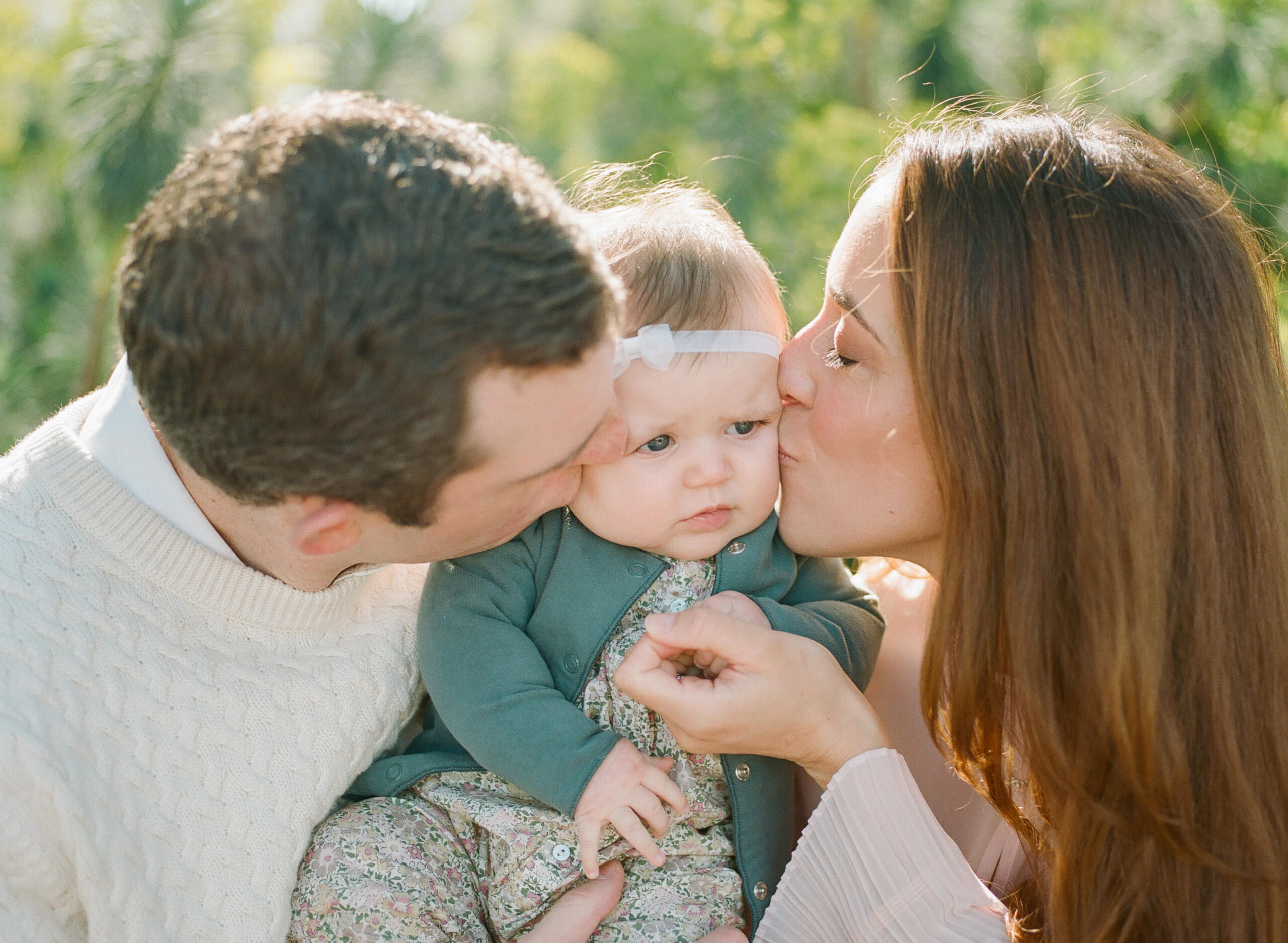 mom and dad kissing the cheeks of baby girl