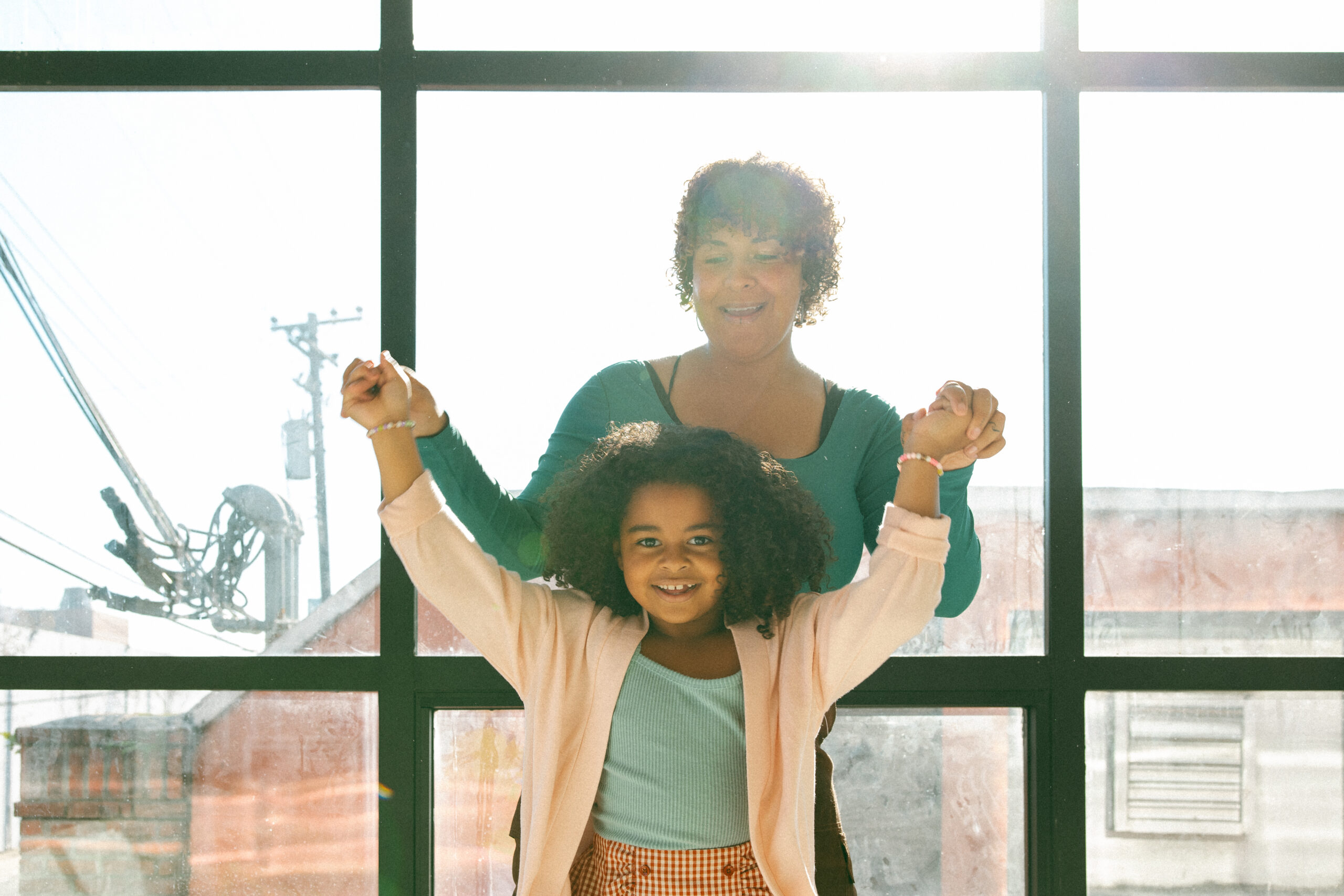 photo of black mom and daughter in front of window dancing