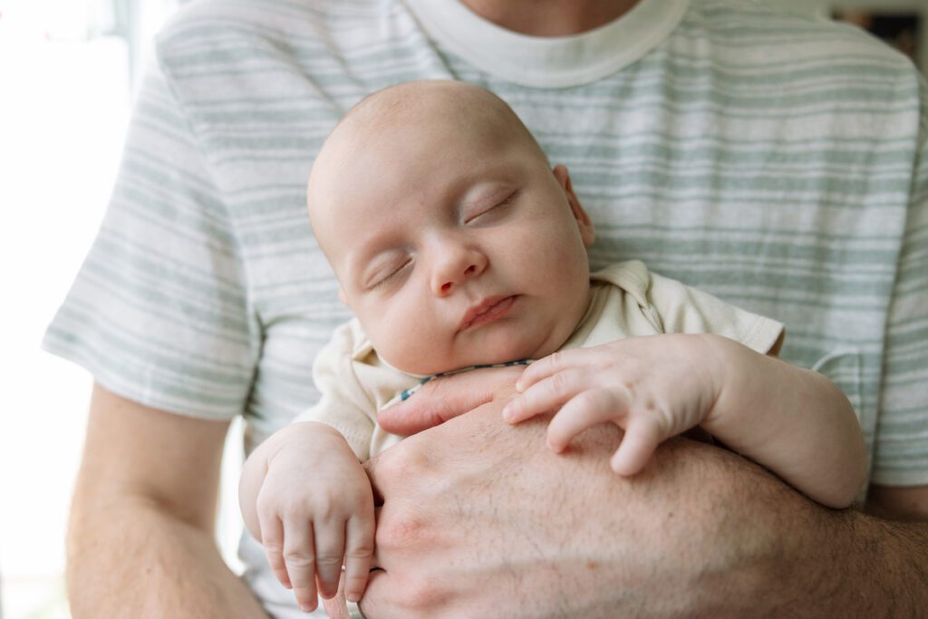 sleeping newborn baby boy being held facing outward by dad