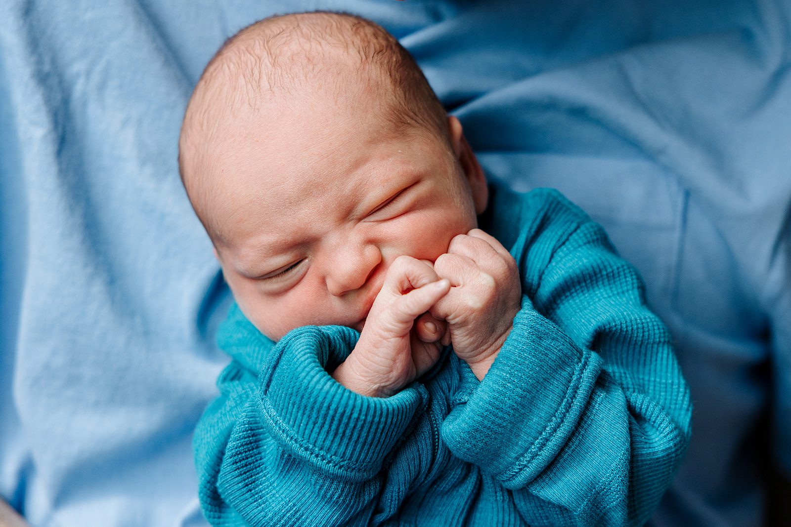 photo of newborn baby boy with fists squished up to his mouth