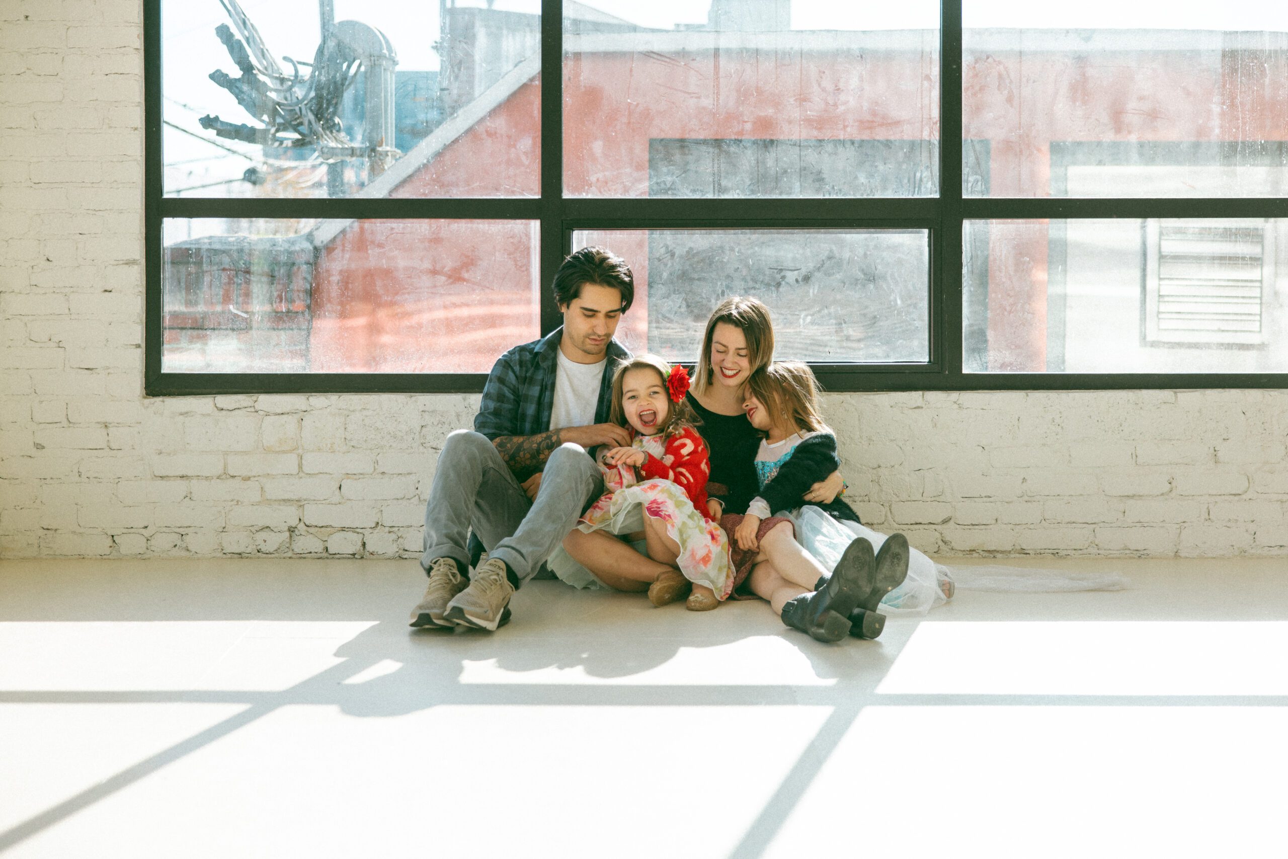 family of four sitting on floor in front of large windows and snuggling together