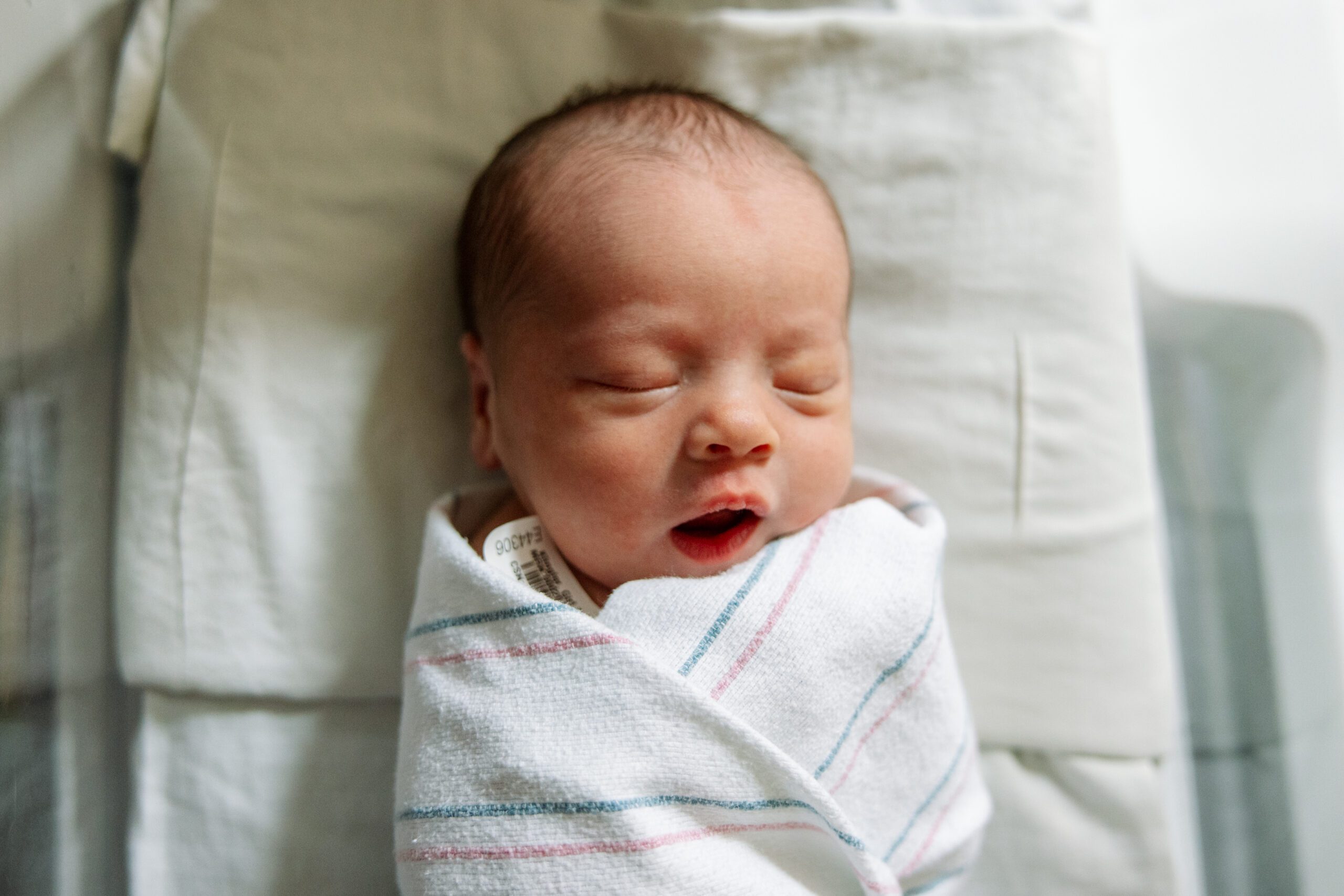 closeup of newborn swaddled in hospital blanket and sleeping in hospital bassinet