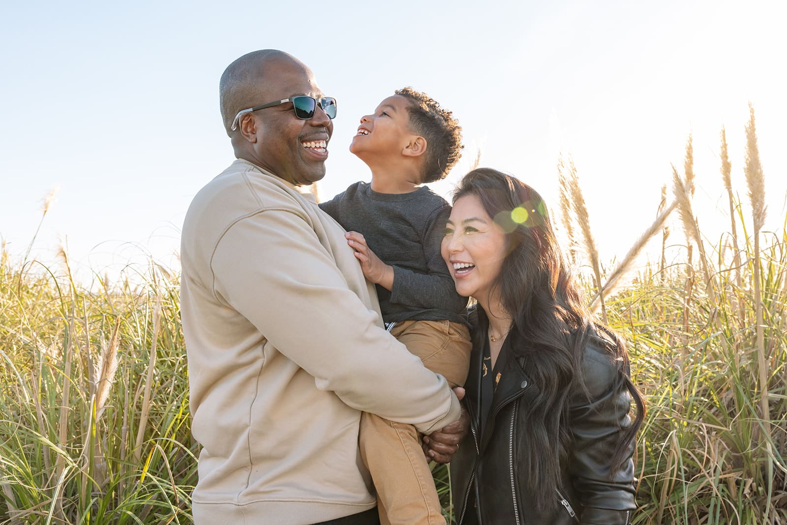 family of three standing in tall grass in late afternoon light and laughing together